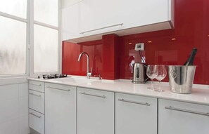 A modern kitchen with a gas stove, a sink, and a red backsplash. - Red Gordon Beach View Apartments + Bomb Shelter (Tel Aviv-Yafo)