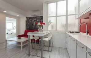A modern kitchen with white cabinetry, a red countertop, and a window with a view. - Red Gordon Beach View Apartments + Bomb Shelter (Tel Aviv-Yafo)
