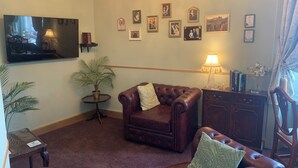 Ein Wohnzimmer mit Ledersofa, Fernseher, einer Kronleuchter und gerahmten Bildern an der Wand.