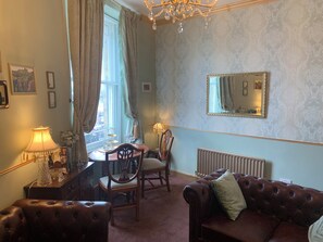 A room with a dining table, chairs, a sofa, a chandelier, a mirror, and a radiator. - Downton I (Alnwick)