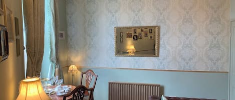 A room with a dining table set for tea, a radiator, a sofa, and a chandelier.