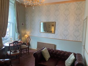 A room with a dining table, chairs, a sofa, a radiator, and a chandelier. - Downton I (Alnwick)