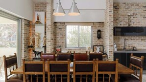 Un coin repas avec un mur en briques, une grande fenêtre et une cuisine moderne en arrière-plan.