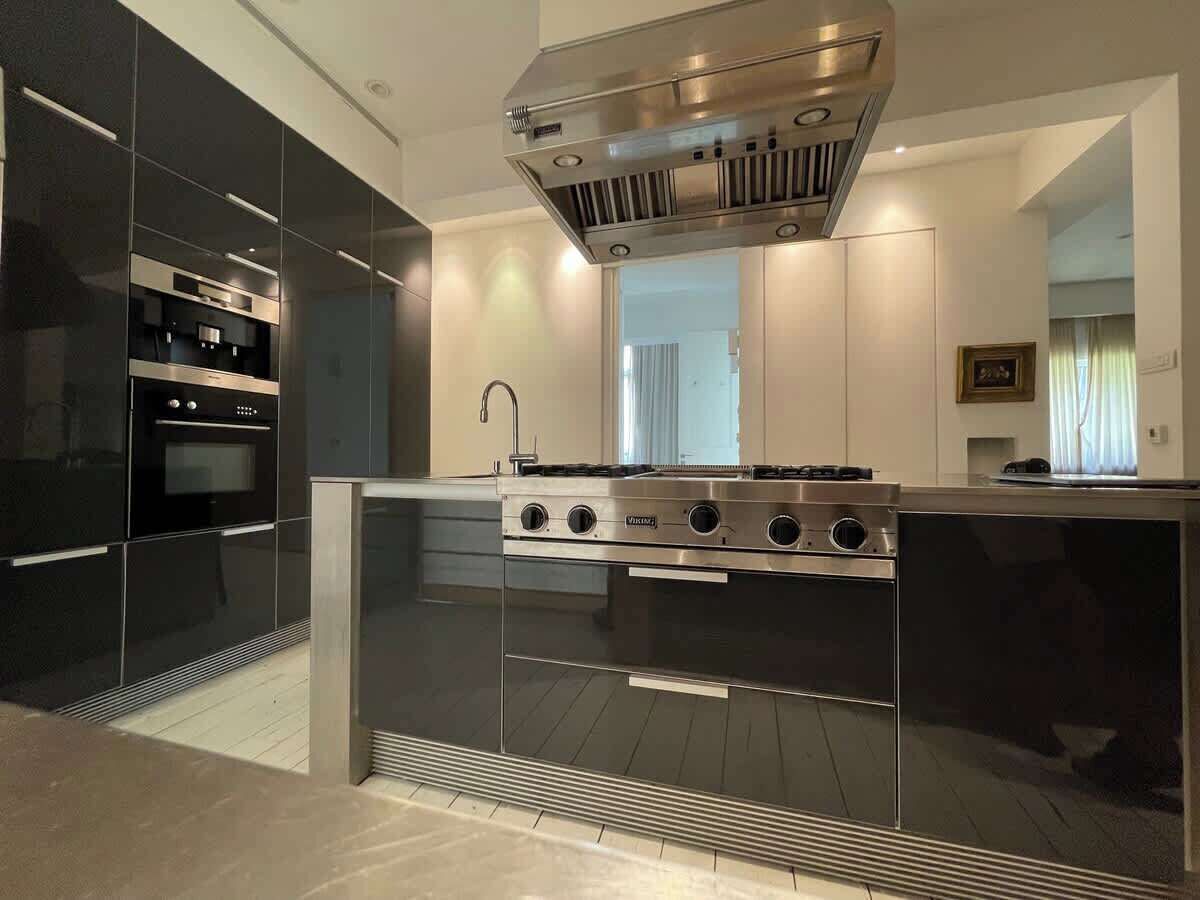 A modern kitchen with a stainless steel stove, black cabinetry, and a large window.