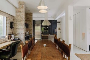 A dining area with a long wooden table, chairs, and pendant lighting. - Gold Gordon Beach Apartments - Chefs apartment (Tel Aviv-Yafo)
