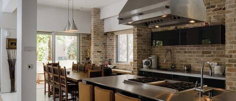 A modern kitchen with a brick wall, stainless steel appliances, and a dining area with wooden chairs.