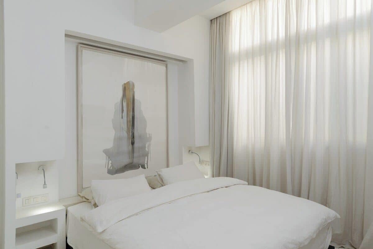 A hotel room with a bed, a nightstand, a mirror, and a window with curtains.