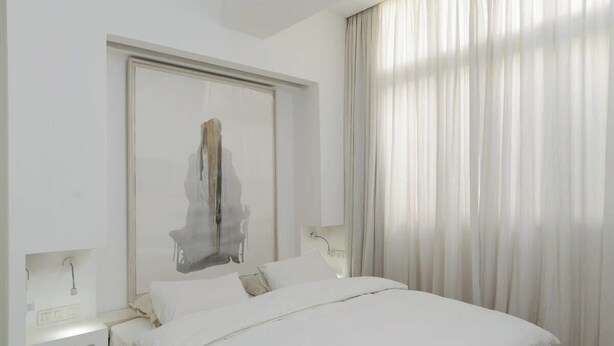 Une chambre d’hôtel avec un lit, une table de chevet, un miroir et une fenêtre avec des rideaux.