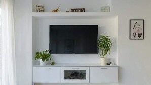 Een witte entertainmentkast met een flatscreen televisie, twee potplanten en een ingelijst beeld aan de muur.