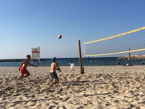 A beach volleyball game with a net and players in the foreground. - Green Gordon Beach View Apartments + Bomb Shelter (Tel Aviv-Yafo)