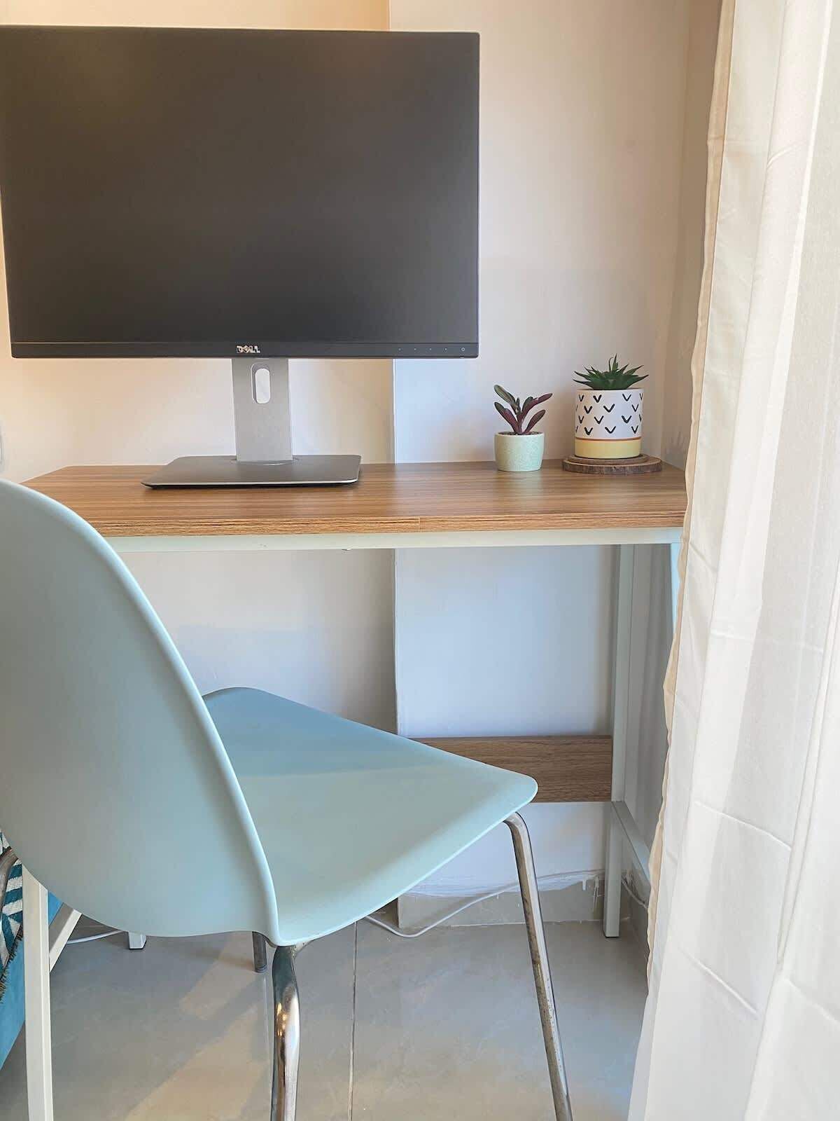 Un espacio de trabajo con un monitor de pantalla plana, una laptop, dos plantas en macetas y una silla azul claro.