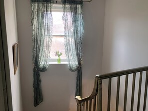 A room with a window covered by sheer curtains, a small vase with flowers, and a wooden railing. - Downton II (Alnwick)