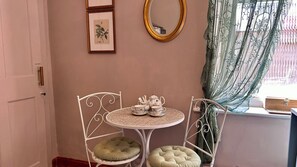 A room with a white metal chair and table, a teapot set, and a framed botanical illustration on the wall. - Downton II (Alnwick)