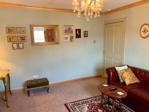 A living room with a chandelier, a red leather sofa, a small table, and a patterned rug. - Downton II (Alnwick)