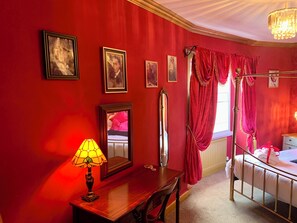 Une pièce aux murs rouges, un lit avec une tête de lit blanche, une table de chevet avec une lampe et un miroir.