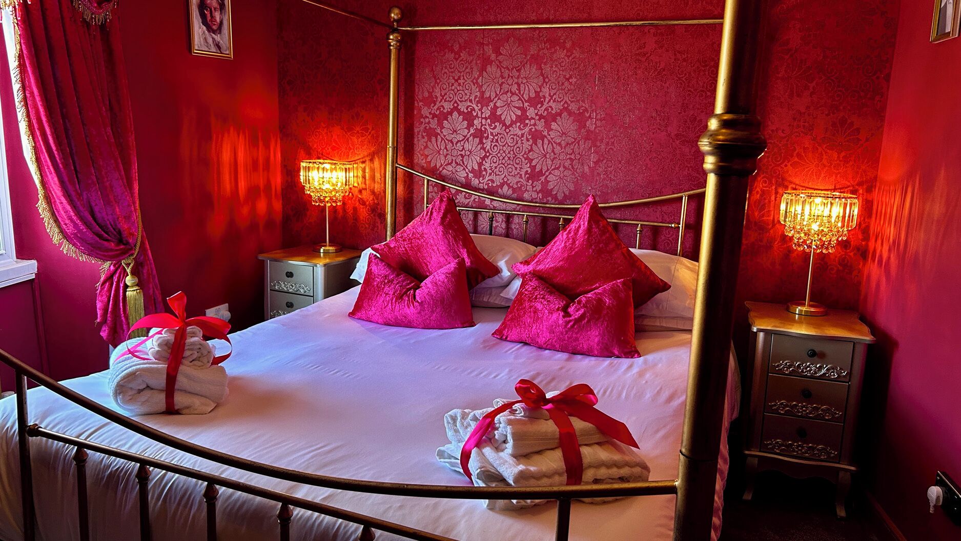 Un lit à baldaquin avec un cadre doré, des oreillers rouges et deux lampes de chevet.