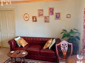 Un salon avec un canapé rouge, une table basse en bois et un fauteuil. Des tableaux encadrés ornent le mur.