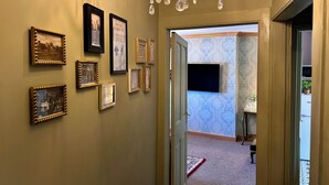 A hallway with framed pictures on the wall, a chandelier, and a door leading to another room with patterned wallpaper. - Downton II (Alnwick)