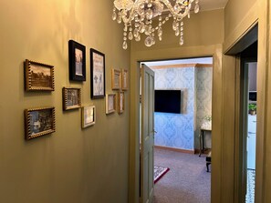 Ein Flur mit gerahmten Bildern an der Wand, einer Chandelierleuchtre und einer Tür, die in einen weiteren Raum mit strukturiertem Wandpapier führt.