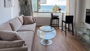 Ett modernt vardagsrum med en soffa, ett soffbord i glas, en matplats med stolar och utsikt över havet.