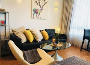 Ein Wohnzimmer mit einer Couch, einem Glastisch, einem Sessel und einem Bücherregal.