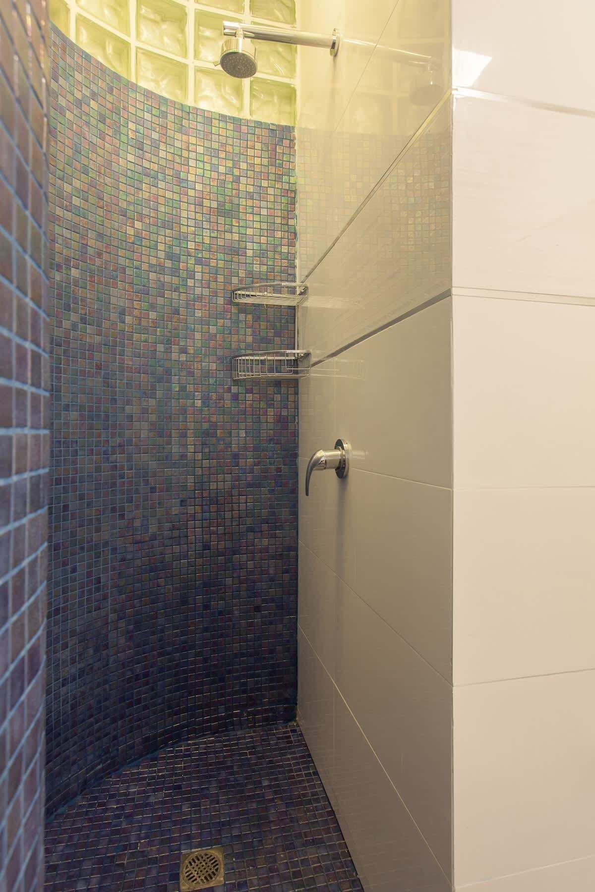 A shower with a tiled wall and a metal showerhead.