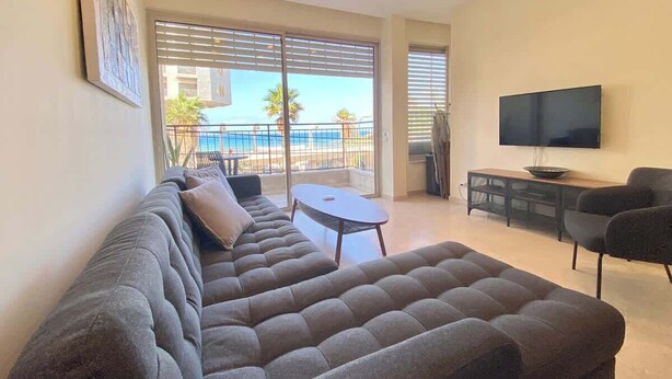 Ein Wohnzimmer mit einem großen Ecksofa, einem Flachbildfernseher und einem Balkon mit Meerblick.