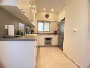 A modern kitchen with white cabinets, a built-in oven, and a stainless steel refrigerator. - White Gordon Beach Apartment + Bomb Shelter (Tel Aviv-Yafo)