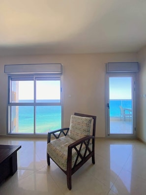 A room with a view of the ocean through large windows, a chair, and a tiled floor. - Krystal View Family 2 parking Bomb Shelter (Bat Yam)