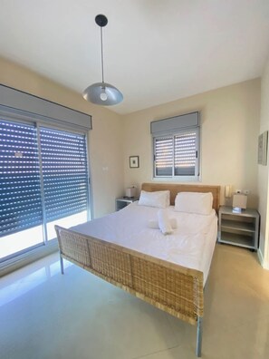 Un dormitorio con cama, mesita de noche, lámpara, luz de techo y ventana con persianas.