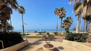 A landscaped area with a central planter, palm trees, and a clear view of the ocean. - Krystal View Family 2 parking Bomb Shelter (Bat Yam)
