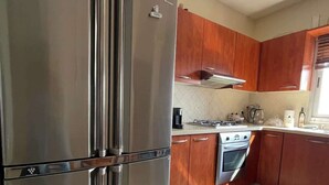 A kitchen with stainless steel appliances, wooden cabinets, and a tiled floor. - Krystal View Family 2 parking Bomb Shelter (Bat Yam)