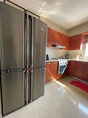 Una cocina con electrodomésticos de acero inoxidable, armarios de madera y piso de baldosas.