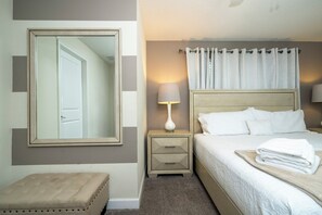 Een hotelkamer met een bed, nachtkastje, lamp, spiegel en een klein krukje.