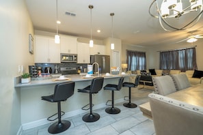 A modern kitchen with a central island, bar stools, and a dining area with a sofa and chairs. - The best 5 bedrooms Storey Lake - 10 min DIsney (Kissimmee)