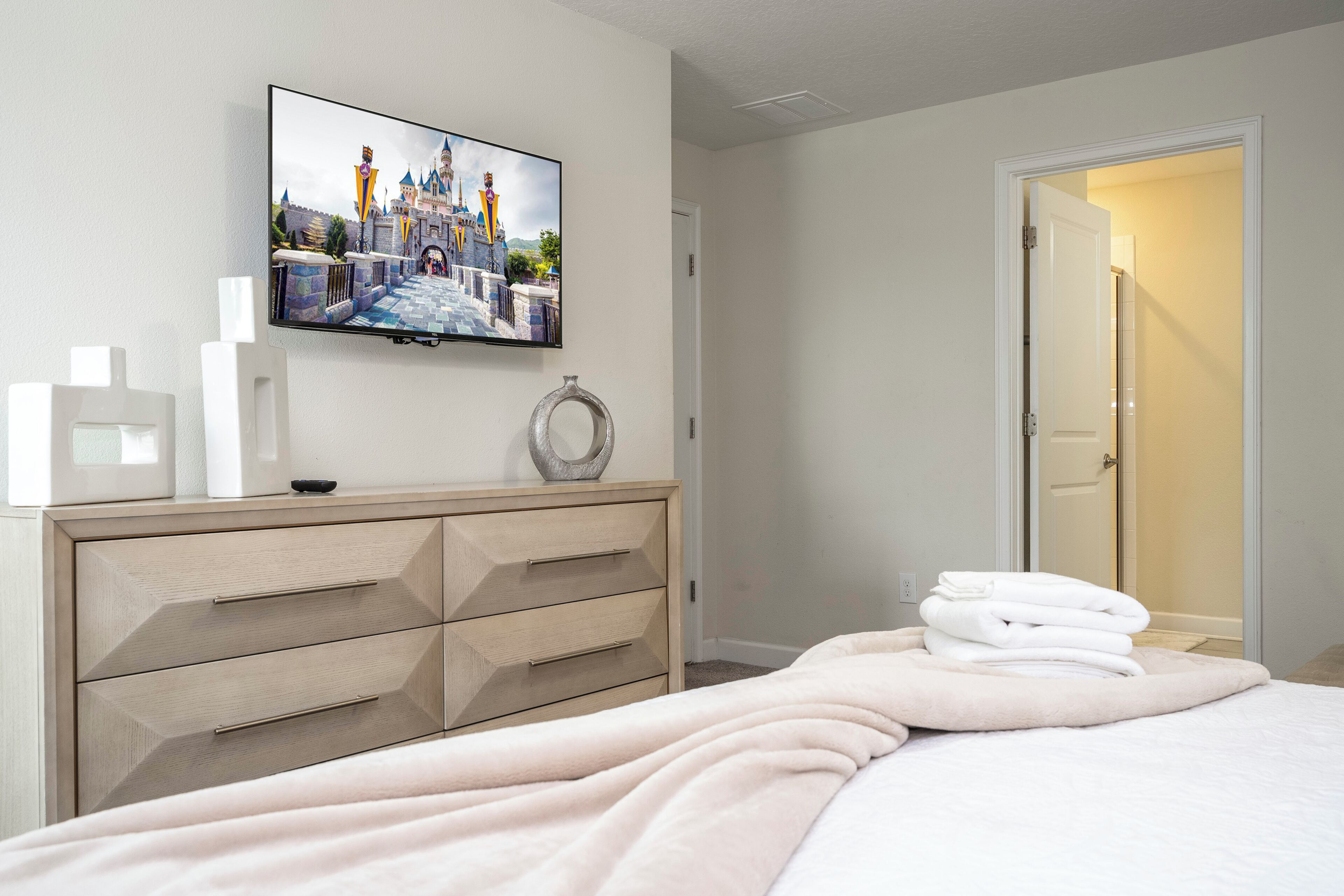 A hotel room with a bed, a TV mounted on the wall, a dresser, and a door leading to another room.