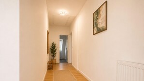 Un pasillo con piso de madera, un tapete, una planta y un cuadro en la pared.
