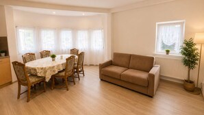 Uma área de refeições com uma mesa redonda e cadeiras, um sofá, uma janela com cortinas e um radiador.