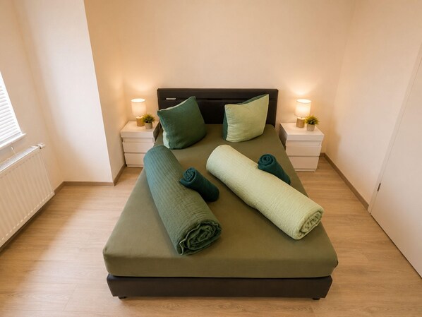 A neatly made bed with pillows and rolled towels, two bedside tables with lamps, and a window with blinds. - Zum Rheinberg - Marksburg Panorama (Braubach)