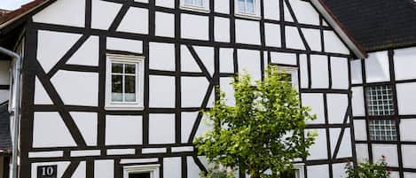 A traditional half-timbered house with a number '10' sign, a wooden picket fence, and a tree in the front yard.
