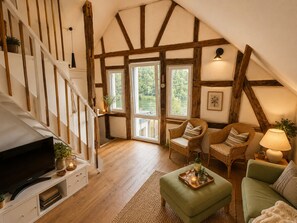 A cozy living room with a wooden staircase, a television, wicker furniture, and a view of the outdoors. - Country House by the Lake - Finkenburg (Waldeck - Nieder-Werbe)