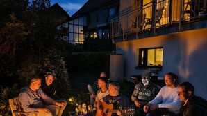 Un groupe de personnes est assis autour d’un foyer à l’extérieur, au crépuscule.