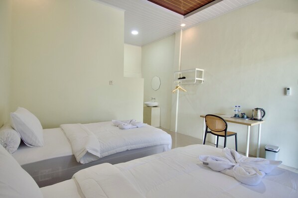 A hotel room with two beds, a desk, a chair, a mirror, and a small table with a kettle and cups.