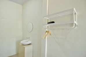 A bathroom with a white sink, a mirror, and a white towel rack with a hairdryer and a pair of wooden hangers. - APA Guesthouse (Labuan Bajo)