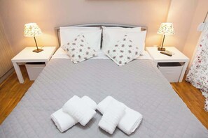 Una cama bien hecha con un edredón acolchado, dos almohadas a juego, dos lámparas de noche y un juego de toallas dobladas sobre la cama.