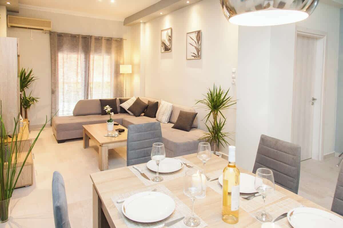 A modern living room with a dining area, featuring a sofa set, a dining table set for four, and a large window with curtains.