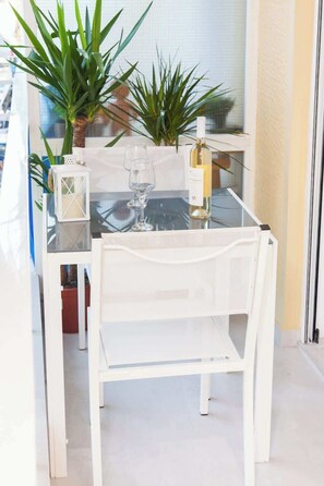 Una mesa de comedor con cubierta de vidrio, una silla blanca, una botella de vino blanco y un candelabro.