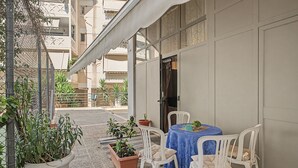 Un área de estar al aire libre con una mesa, sillas, plantas en macetas y un edificio al fondo.