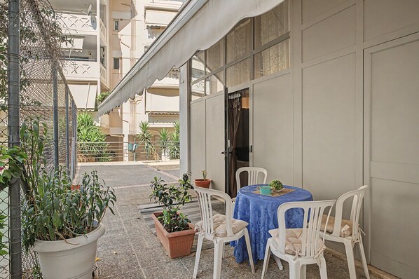 A covered outdoor seating area with a table and chairs, potted plants, and a building in the background. - Maria's Nest Studio in an Ideal Central Athens Location (Athens)