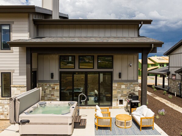 A modern outdoor patio with a hot tub, wicker furniture, and a stone fireplace. - Relax. Recharge. Repeat in DVE, Hot Tub, Pet Friendly (Heber City)